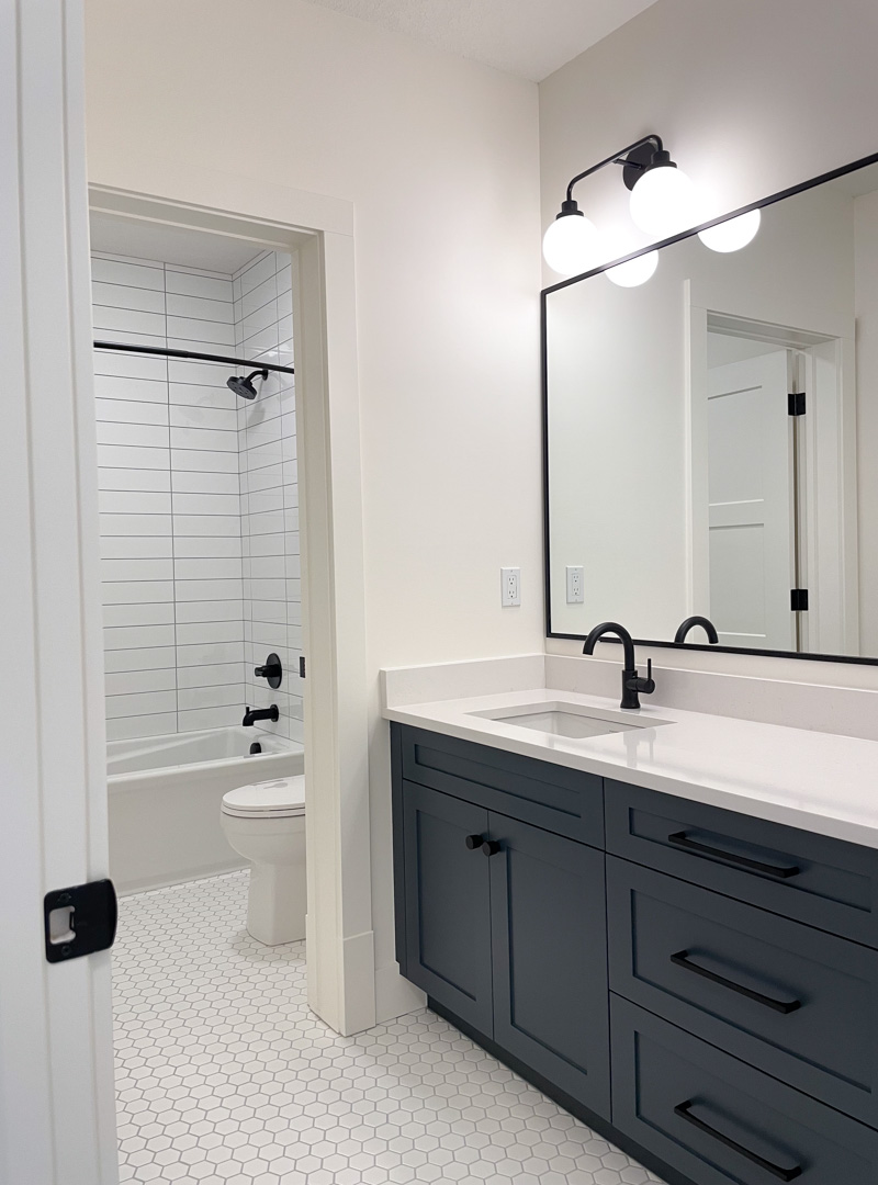 Modern Vintage Bathroom with White Hexagon Tile Floor, Dark Navy Cabinets and Matte Black Hardware