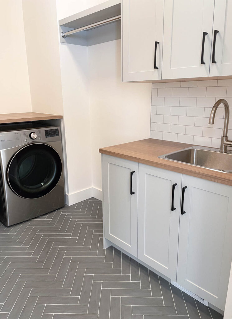 Laundry Room with Dark Grey Herringbone Tile Floor, Light Grey Cabinets and Matte Black Hardware