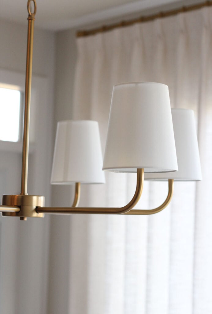 6-light brass chandelier with white shades hanging in dining room