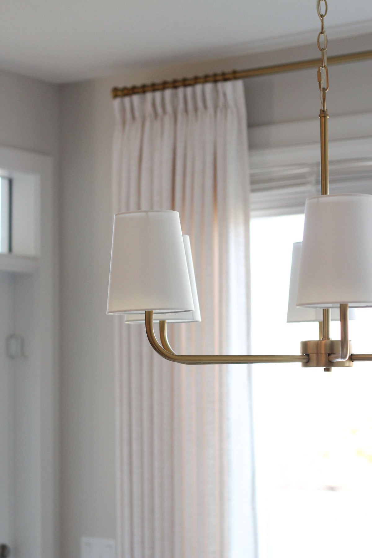 Close-up of open arm brass chandelier with white fabric shades hanging in dining room