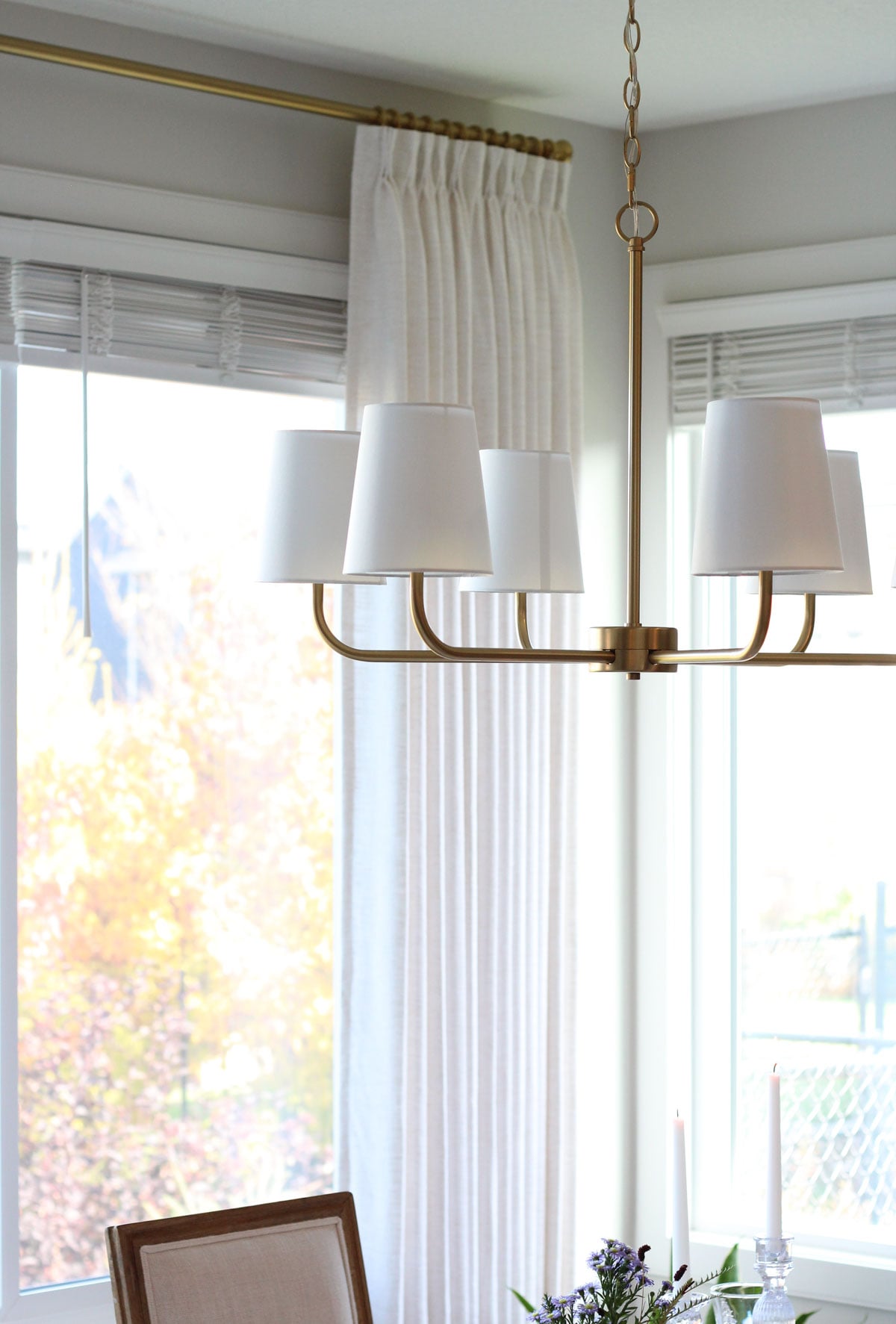 Brass chandelier with white shades hanging over dining table