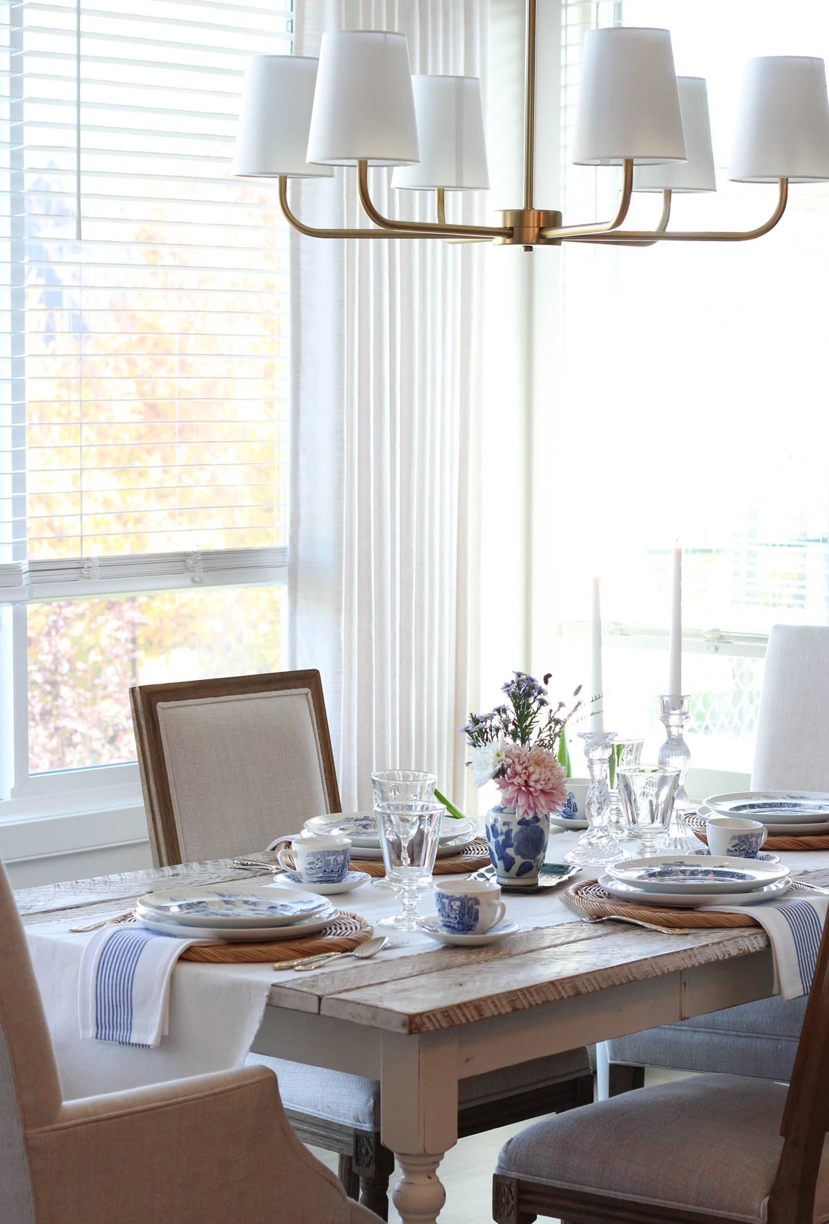 Dining room with beige white linen curtains, brass chandelier and whitewashed table