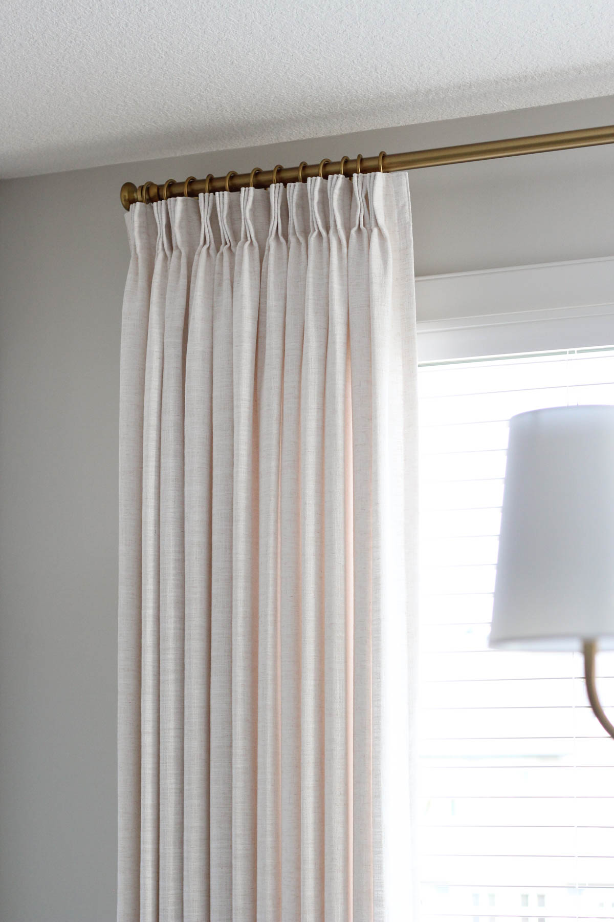 Beige white linen drapery hung from brass curtain rod with rings